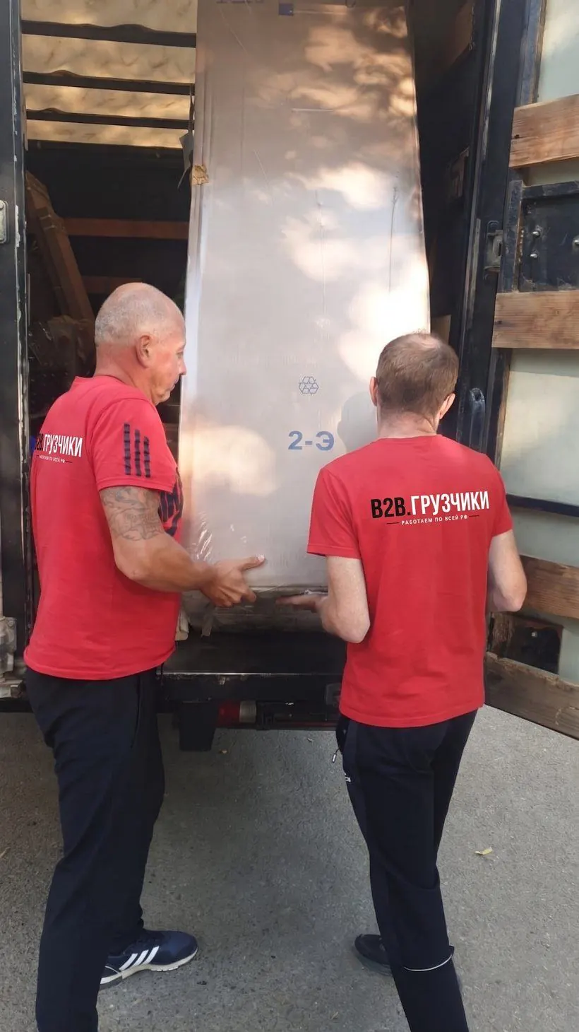 Двое грузчиков загружают мебель в машину